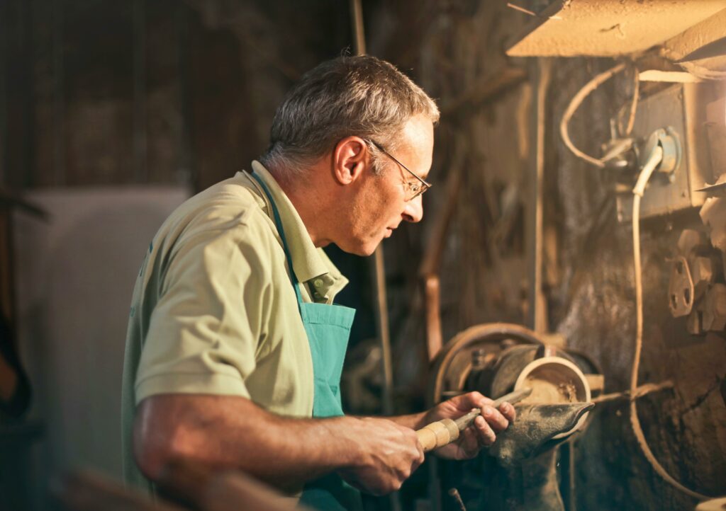 A senior craftsman focuses intently while working with tools in a dimly lit workshop.